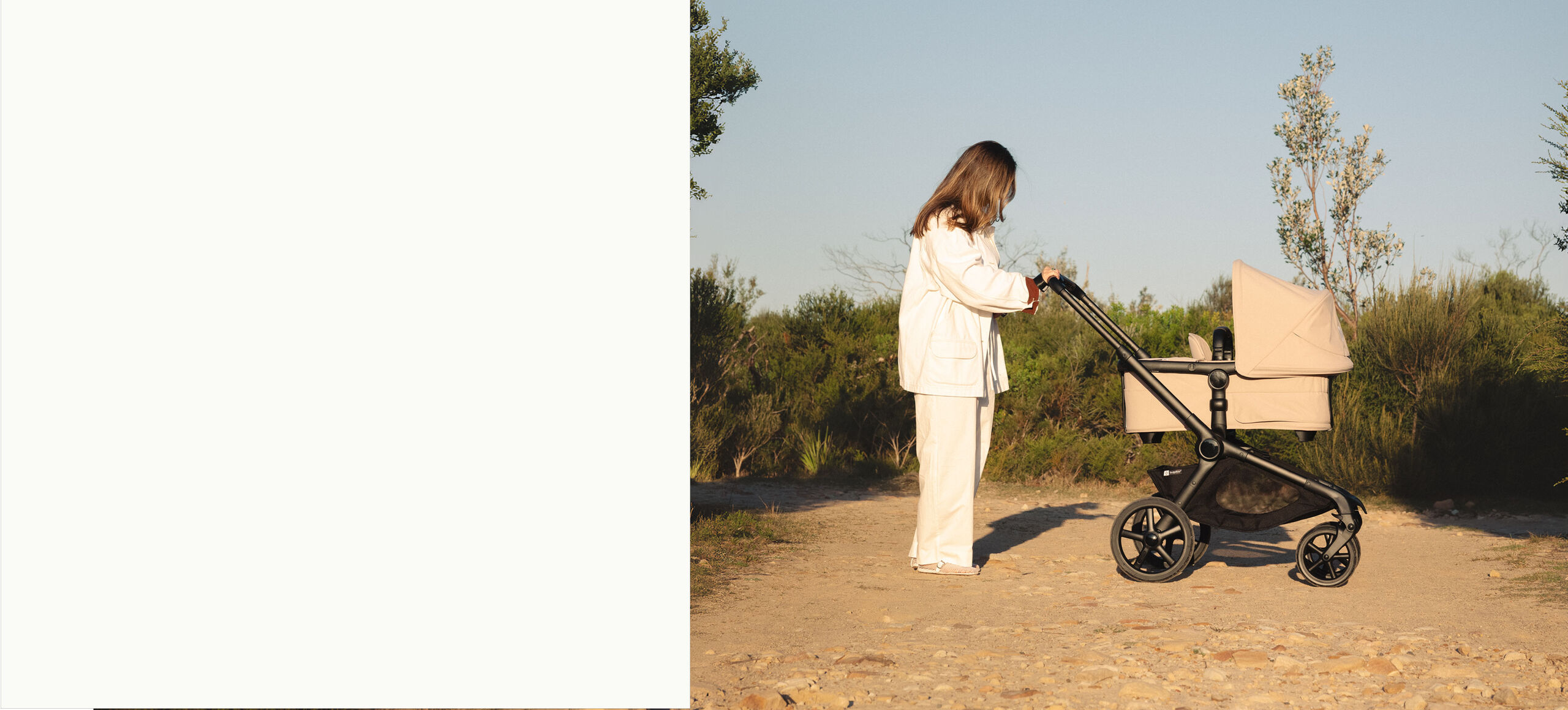 Parent pushing the Bugaboo Kangaroo pram in Desert Beige along a sunny countryside path surrounded by trees and greener.