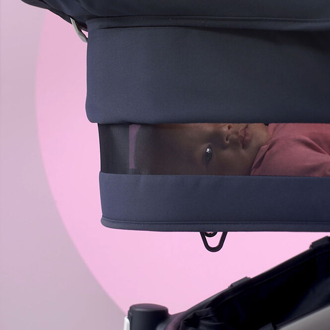 A baby peeking through the ventilation panel of the Bugaboo Donkey 5 breezy bassinet.