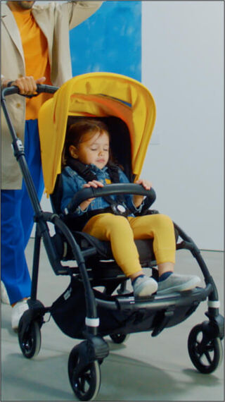Toddler sitting in a Bugaboo Bee 6 while parent pushes her around in a gallery.
