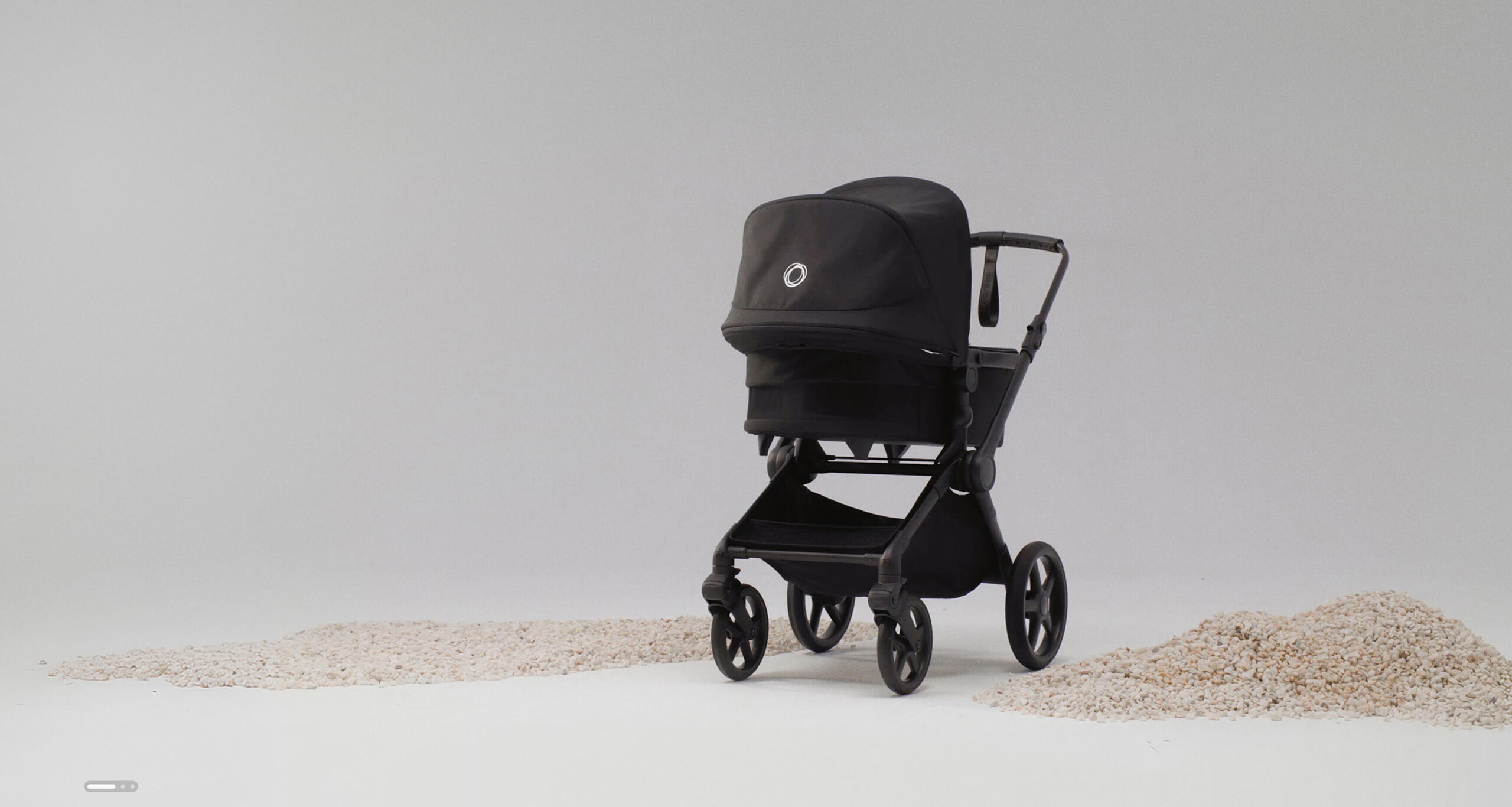 A Bugaboo Cub all-terrain stroller in black fabrics inside a studio space, next to piles of sand on the ground.