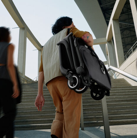 A dad carries a folded Bugaboo compact stroller on one shoulder as he heads towards the stairs.