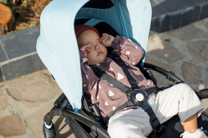 : Ein Baby reibt sich die Augen nach dem Schlafen in einem Bugaboo Kinderwagen.)