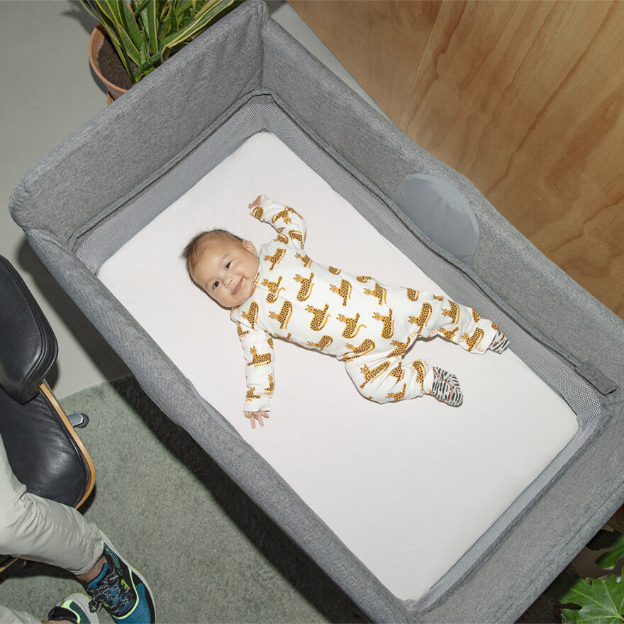 Bird’s eye view of a baby in an animal print romper, lying in the Bugaboo Stardust travel cot.