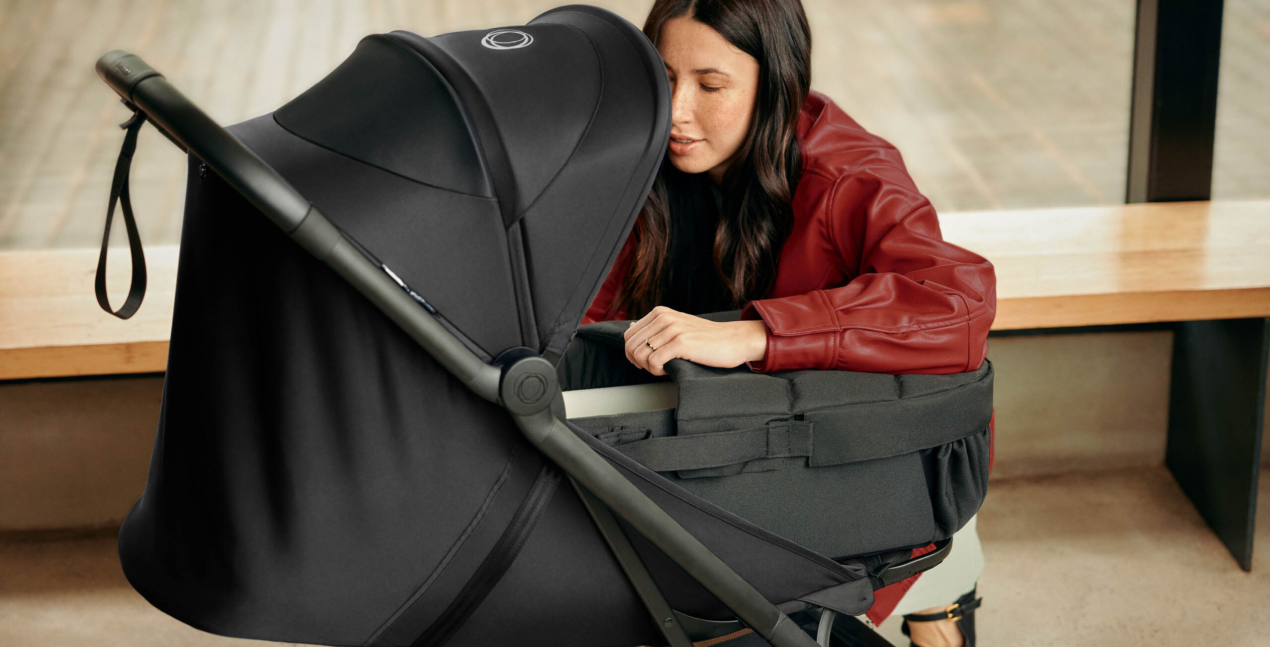 A mother leans over to look inside a Bugaboo baby nest on a Bugaboo Butterfly 2 travel pushchair with black fabrics.