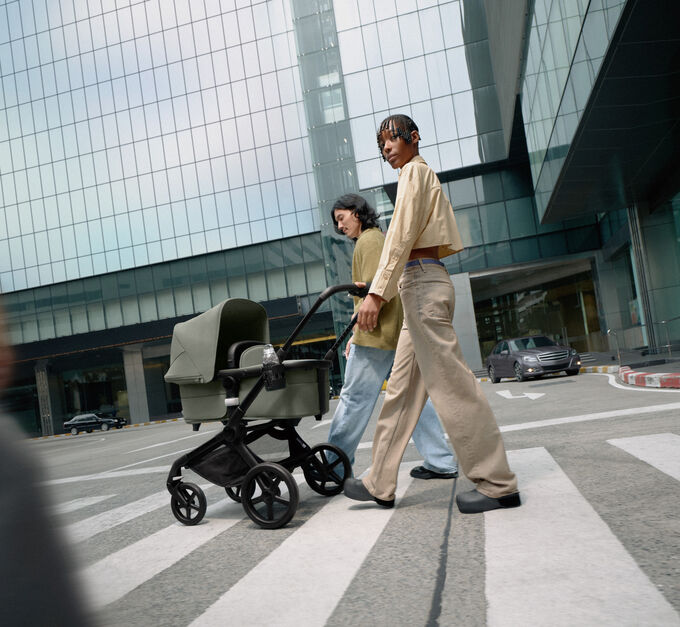 Una coppia elegante cammina con passo sicuro con il loro neonato in un passeggino Bugaboo Fox 5. Attorno a loro sorgono grattacieli di vetro.