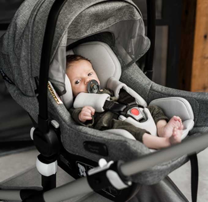 A young baby sitting in a grey Bugaboo Turtle Air by Nuna car seat