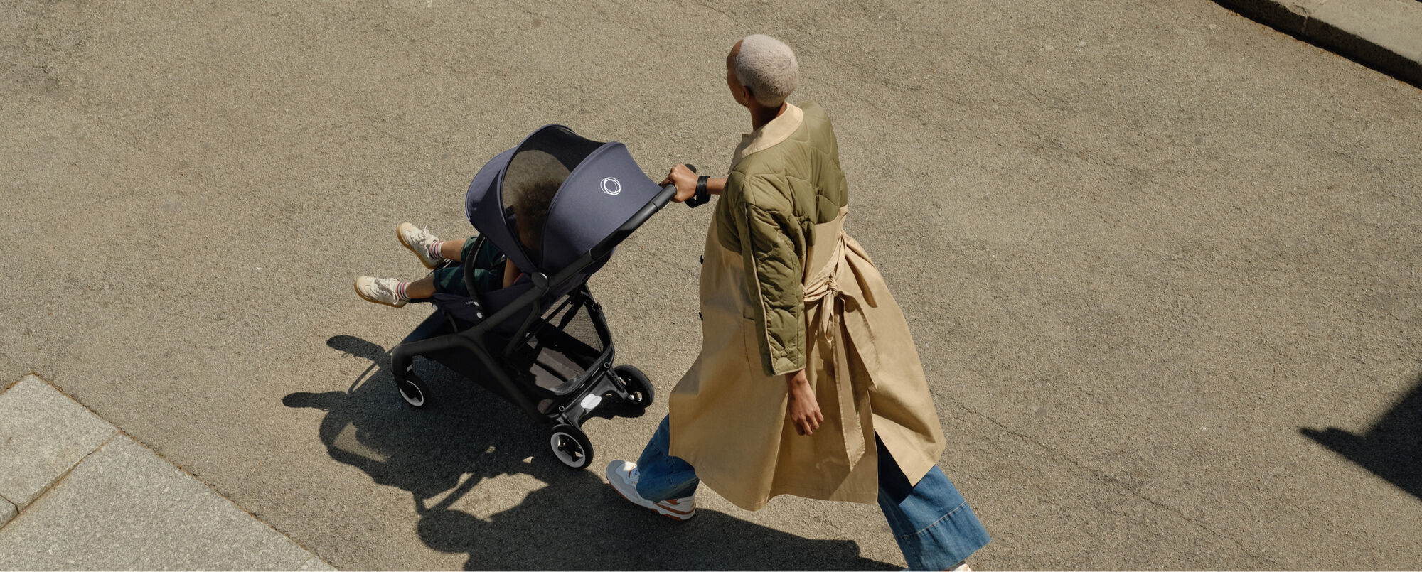 A stylish mom pushing a Bugaboo stroller on the street.	 	 	