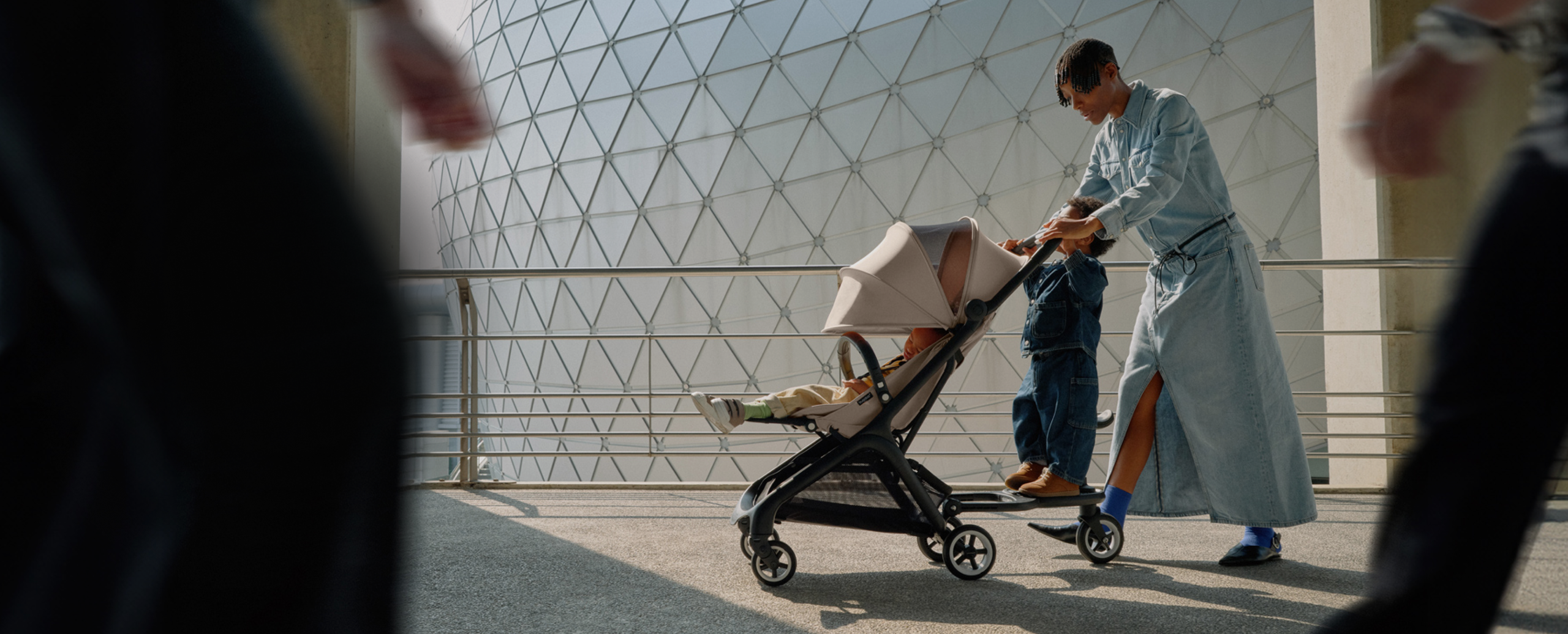 A stylish couple take confident strides with their newborn in a Bugaboo Fox 5 stroller. They're surrounded by glass skyscrapers.