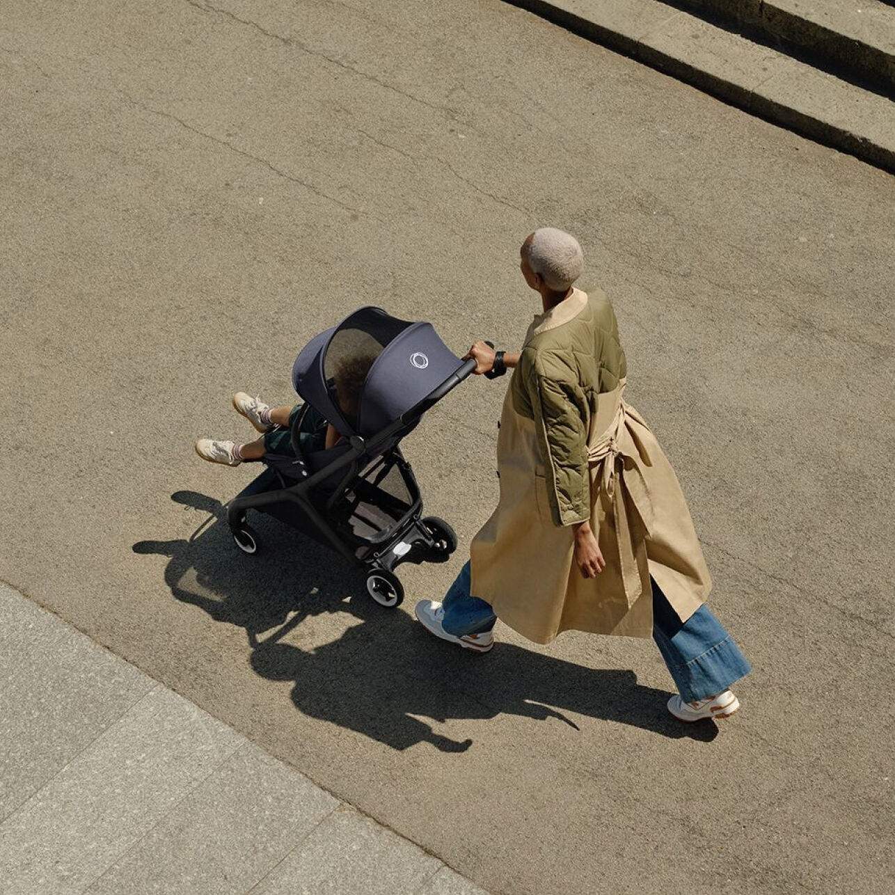 부가부 버터플라이 컴팩트 여행용 스트롤러에 타고 있는 아이와 함께 자신 있게 걷고 있는 엄마.