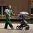 Mom carrying baby in one arm while pushing a Bugaboo Fox 5 stroller decked with multiple accessories. - Thumbnail Slide 12 of 12