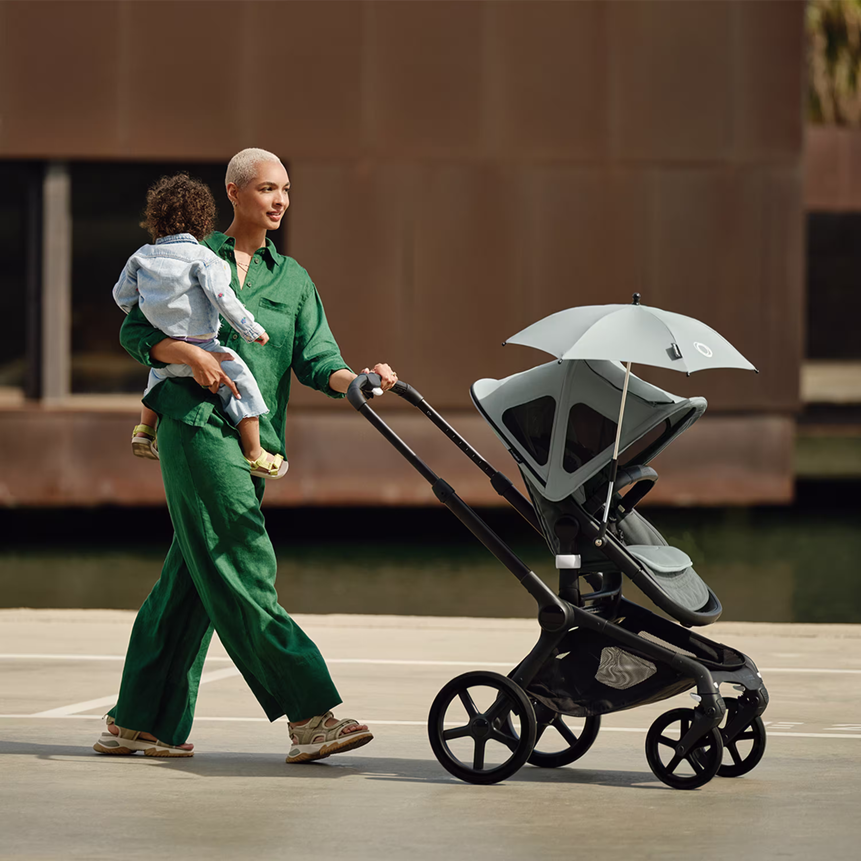 Mom carrying baby in one arm while pushing a Bugaboo Fox 5 stroller decked with multiple accessories. - Main Modal Image Slide 12 of 12