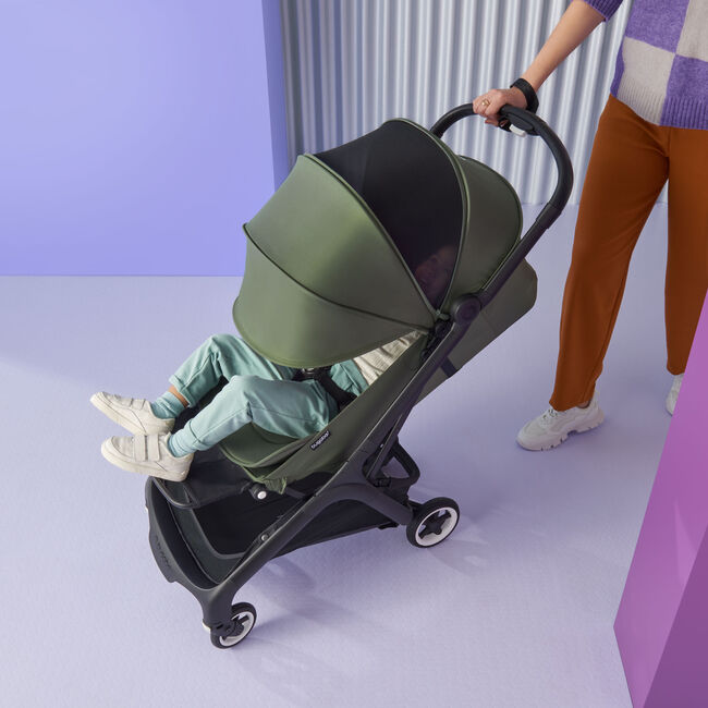 Mom pushing a Bugaboo Butterfly stroller with baby napping inside; the sun canopy is fully extended, showing the breezy panel.