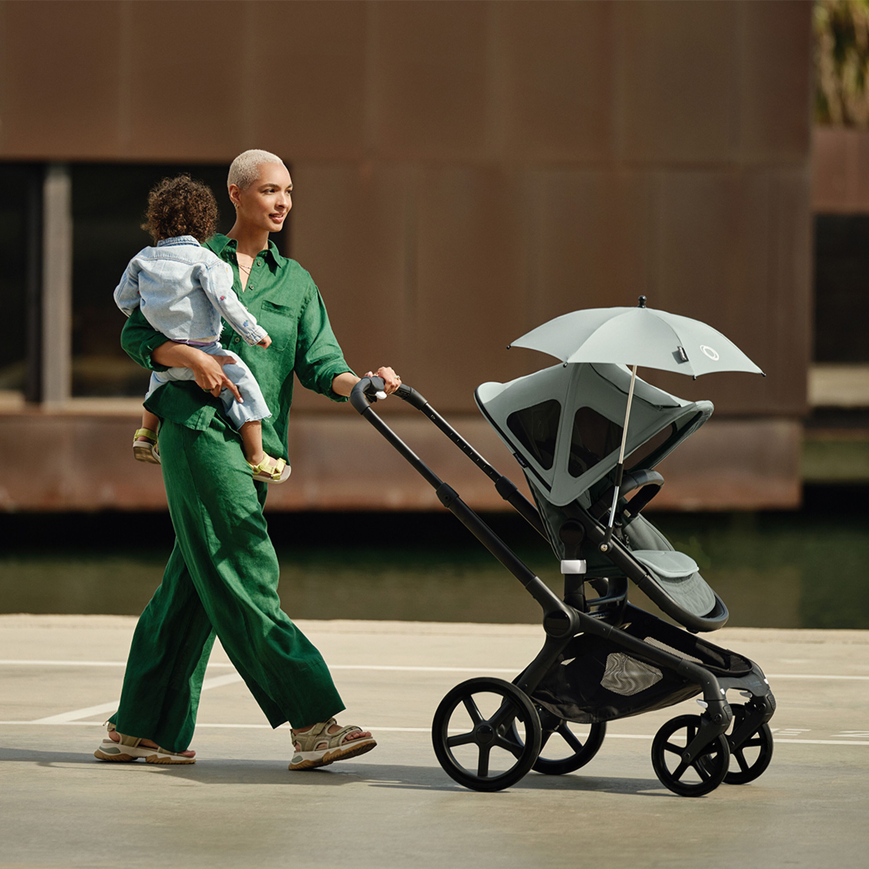 Mom carrying baby in one arm while pushing a Bugaboo Fox 5 pushchair  decked with multiple accessories. - Main Modal Image Slide 12 of 13
