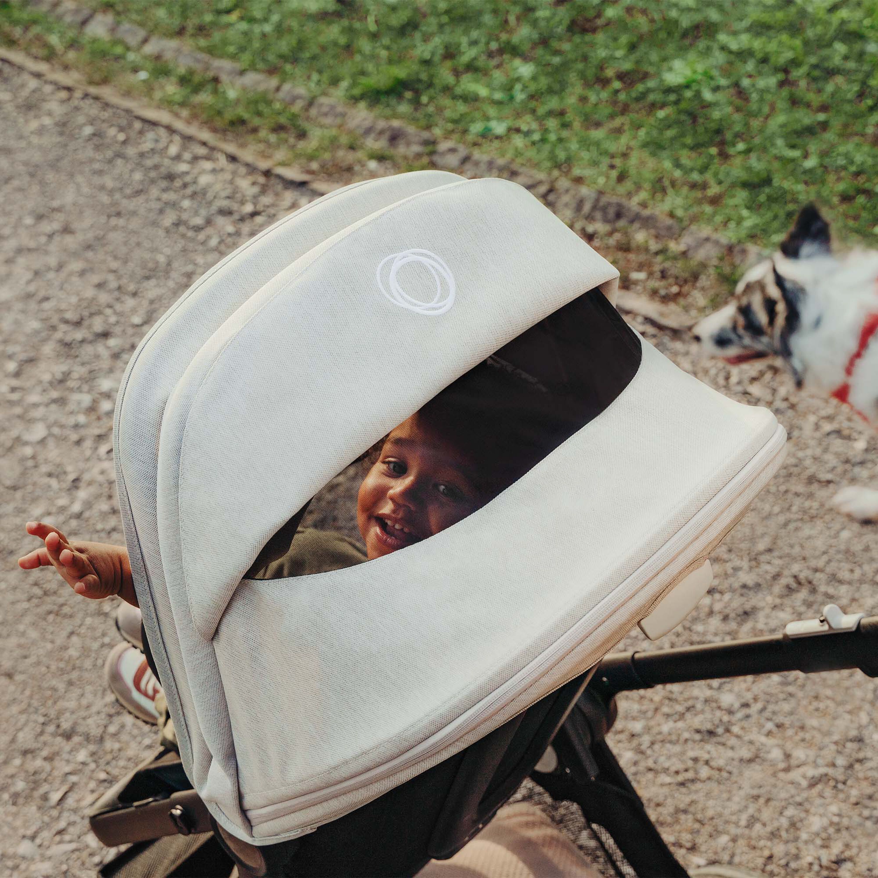 Smiling baby looking through the peekaboo panel of a white Bugaboo sun canopy. - Main Modal Image Slide 3 of 3