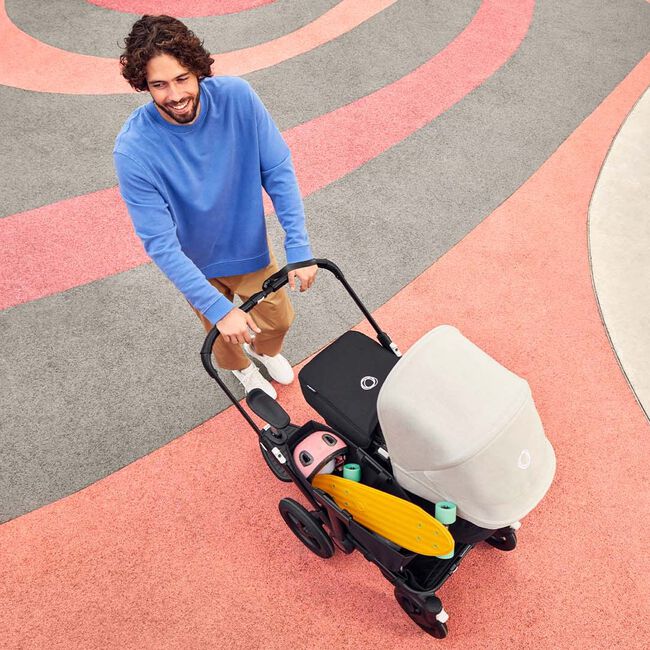 Dad strolling with the Bugaboo Donkey 5 Mono stroller with white sun canopy and side luggage basket filled with toys.