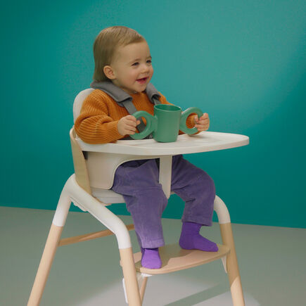 Toddler in a Bugaboo Giraffe chair with white baby set and white tray.