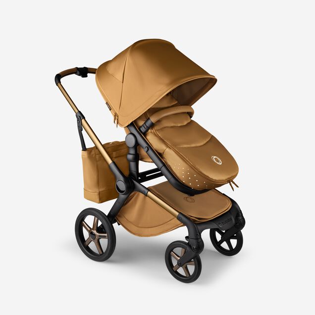 A Bugaboo Fox 5 Noir Limited Edition stroller with a footmuff and changing bag, all in the Amber Glow colorway. - Main Image Slide 15 of 15