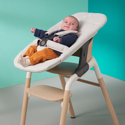 Baby in a Bugaboo Giraffe chair, with newborn set in white fabrics. - view 2