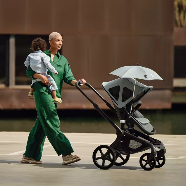 Mom carrying baby in one arm while pushing a Bugaboo Fox 5 pushchair  decked with multiple accessories. - Main Image Slide 12 of 13