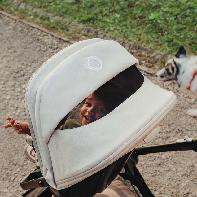 Smiling baby looking through the peekaboo panel of a white Bugaboo sun canopy. - Main Image Slide 3 of 7