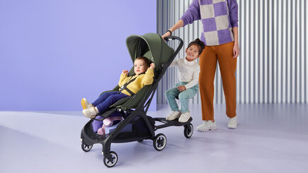 Mutter, die den Bugaboo Butterfly Kinderwagen schiebt, während das Baby im Kinderwagen und das Kleinkind auf dem Bugaboo Butterfly Komfort-Mitfahrbrett + sitzt. 