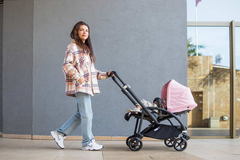 Young mom walking with her baby in a pink and black stroller