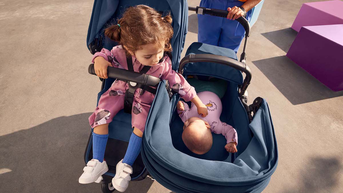 Older sister sweetly touches little sister while in a side-by-side double stroller